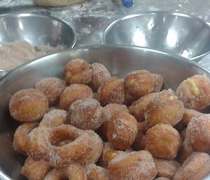 A big bowl of freshly mad donuts covered with sugar.