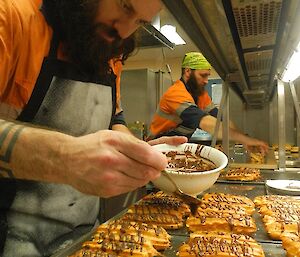 Adam drizzling chocolate over a tray of chocolate éclairs.