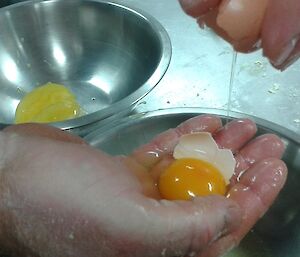 Close up photo of an egg being separated into white and yoke using fingers as a strainer