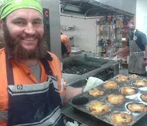 AJ smiling and holding up a tray of Portuguese tarts hot from the oven.