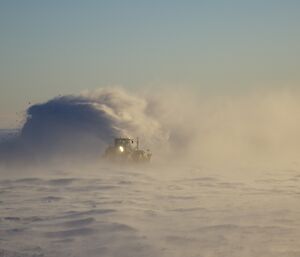 The large snow blowing machine in the distance in a cloud of snow.