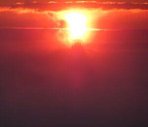 A fire ball sunset with a faint outline of a snow blower in action.