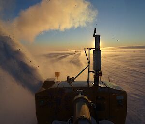 Photo taken from the driver’s seat of the snow blower with the sun behind the exhaust pipe on a blue sky background.