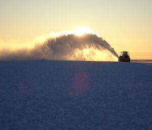 The snow blower in the distance with a bloom of snow covering the sun.