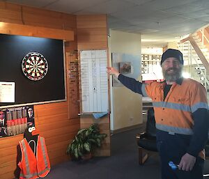 Cam is throwing a dart at the dart board, looking back towards the camera & smiling.