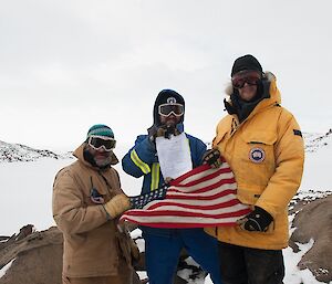 Three expeditioner holding the American flag and official document that was left in the cylinder at the monument