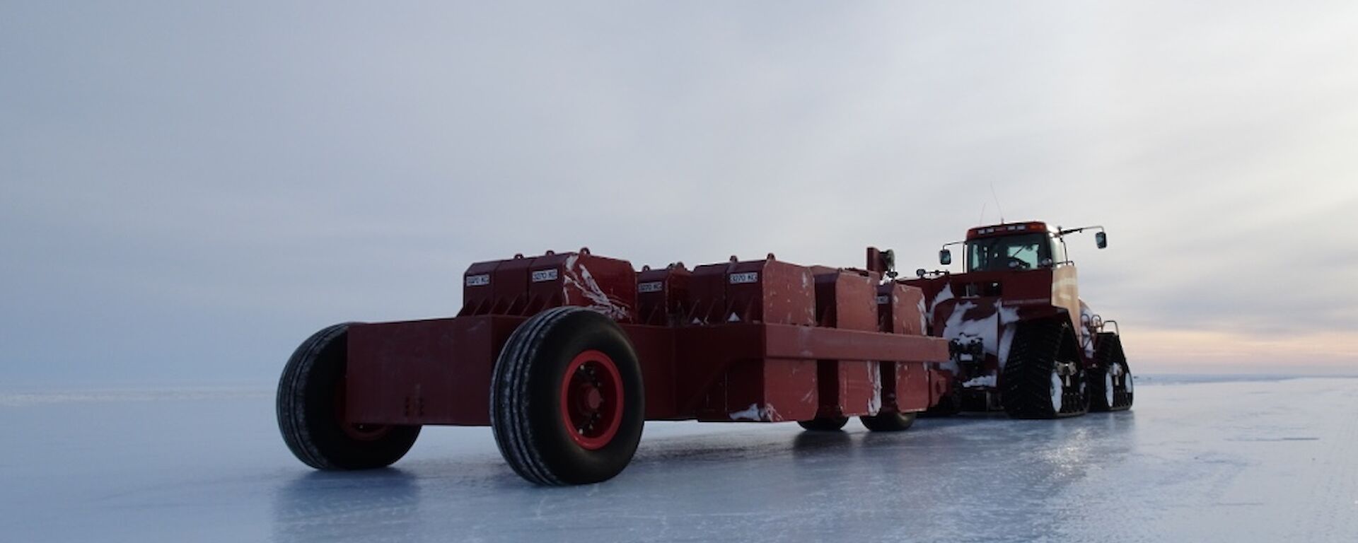 The QuadTrac tractor hooked up to the long red proof roller which is parked on the blue ice runway.