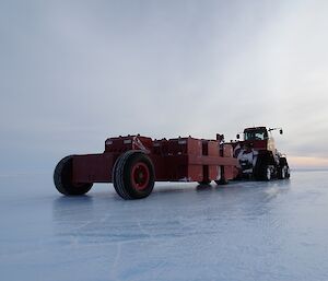 The QuadTrac tractor hooked up to the long red proof roller which is parked on the blue ice runway.