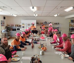 Expeditioners sitting and standing around the tables wearing pink hard hats and clothing as they enjoy their morning tea.