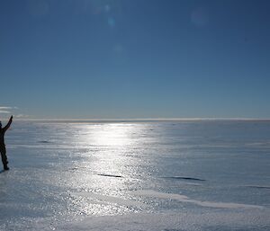 Expeditioner standing on the blue ice with his arm up in the air on a bright sunny day.