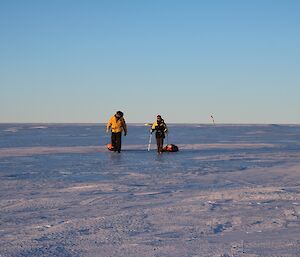 Two expeditioners walking on the blue ice towards the camera with both towing a small sled with their survival pack on the sled.