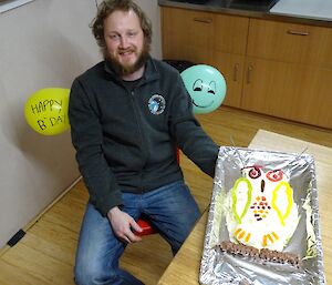 Peter sitting with his birthday cake which is in the shape of an owl.