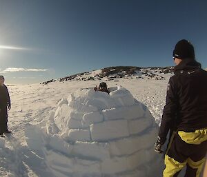 An ice block igloo with person pocking their head through the top