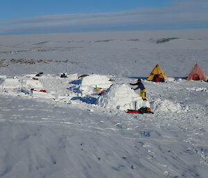 People building ice shelters with tents in background
