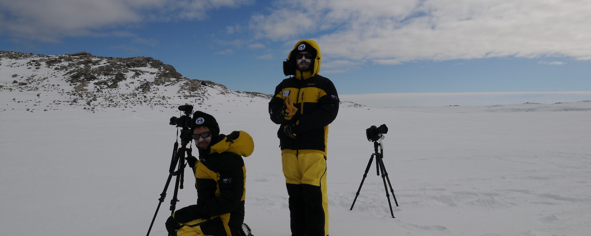 Two journalists stand by a movie camera in the Antarctic wilderness