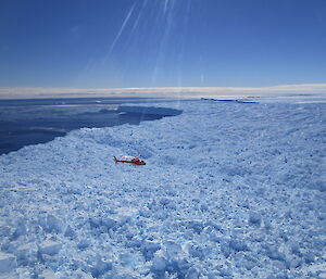 A helicopter flies over a rough glacial landscape