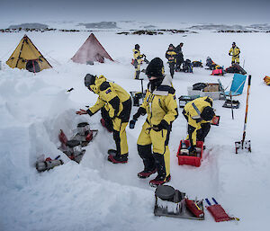 A group of expeditioners preparing dinner on a small stove on a snow ledge during field training.