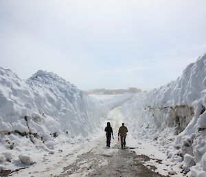 Two expeditioners walk along a snow cleared roadway