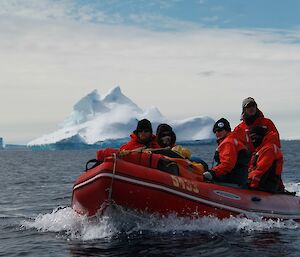 A boat load of expeditioners in the foreground of a large ice berg