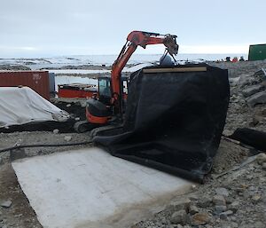 A backhoe covers up the matting in the bio pile
