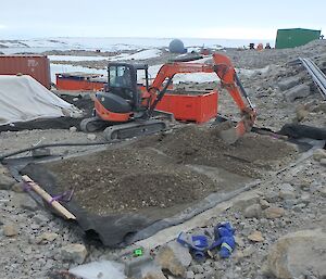 A backhoe scrapes soil to cover the matting