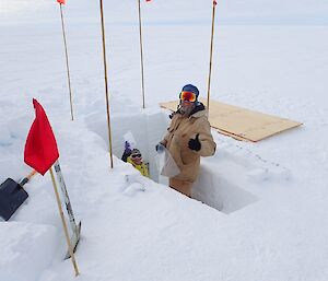 An expeditioner assists with the bagged samples, standing in an ice trench