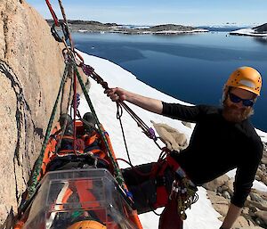An expeditioner is lowered down a rock face during SAR training
