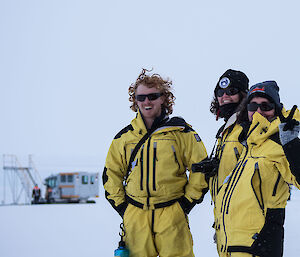 Three expeditioners in yellow suits smiling at camera