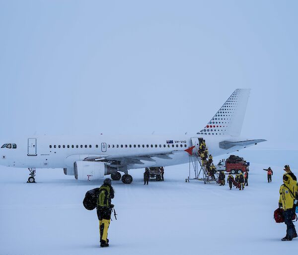 The A319 aircraft on the ice runway being boarded by expeditioners in yellow suits