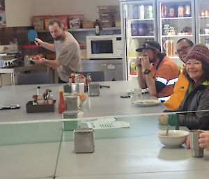 Expeditioners eating lunch on a table with a table tennis net across it.