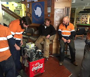 Group of expeditioners in high viz work clothes looking at a coke machine on the floor