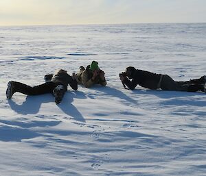 Three expeditioners laying on the snow taking photos