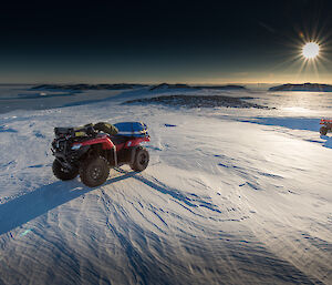 Two quad bikes on snow with sun in background