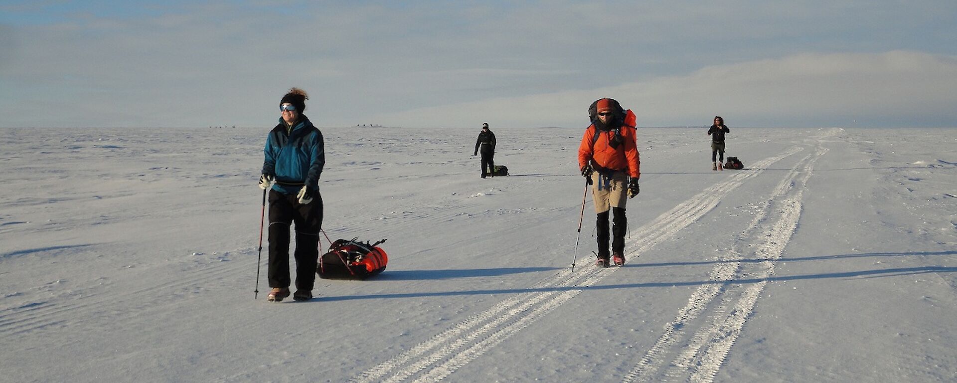 4 hikers dragging sleds walking along a snow road