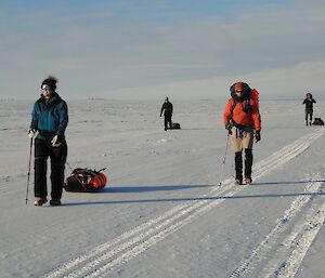 4 hikers dragging sleds walking along a snow road