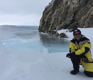 Andrew kneeling in front of rocks on blue ice