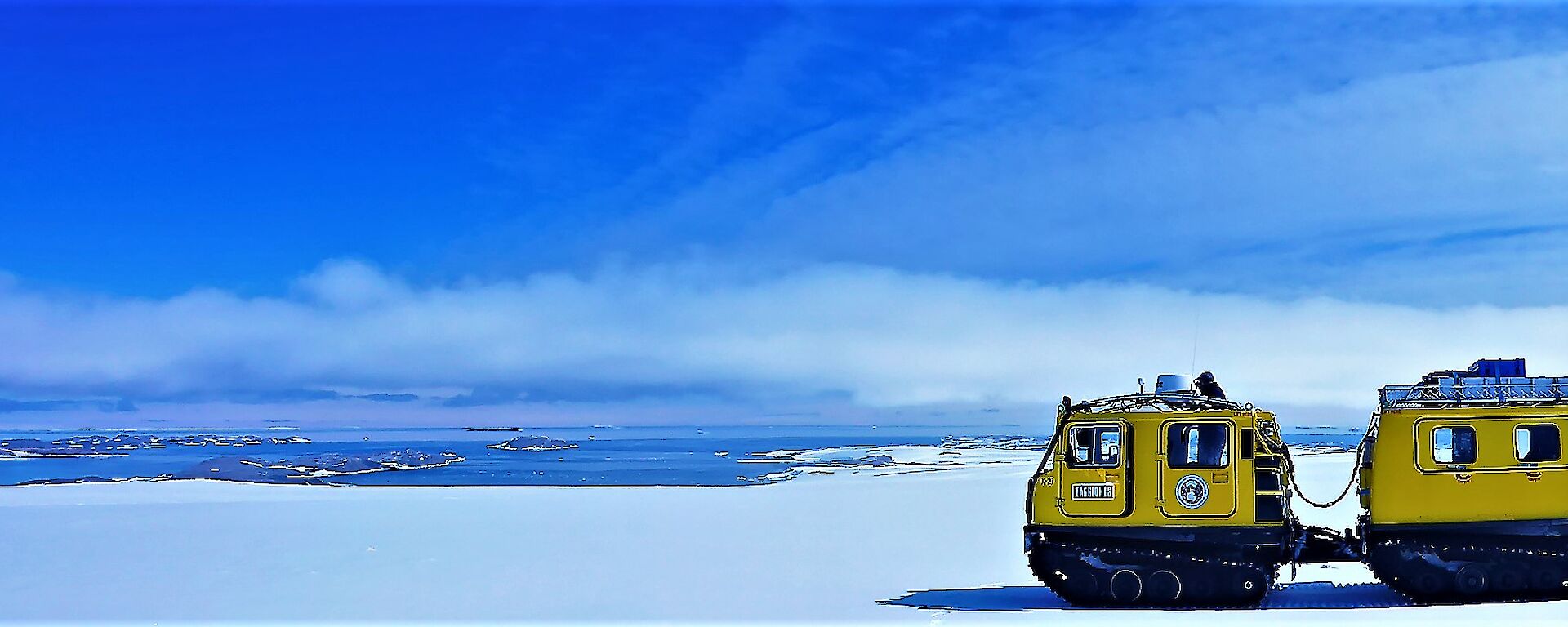 Yellow Hägglunds on snow with blue sky