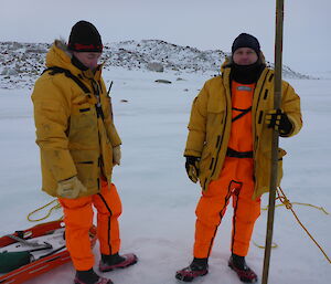 Two expeditioners in drysuits and yellow jackets one holding a pole