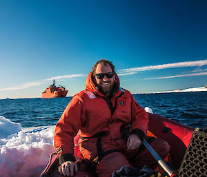 Simon sitting in boat with ship in background