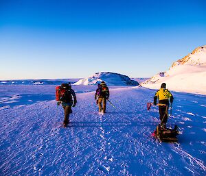 Three expeditioners walking on sea ice away from camera