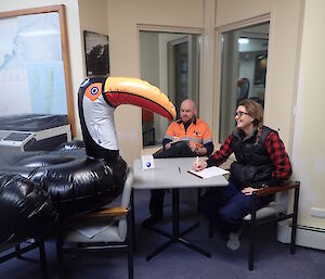 Two expeditioners sitting at table with inflatable toucan