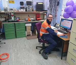 Clint at desk with bunch of purple balloons on desk