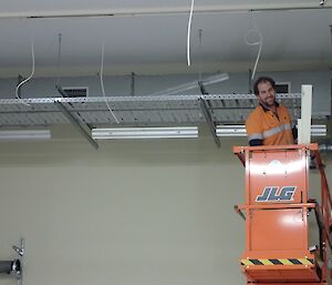 A man in the scissor lift near the ceiling of a building with wires hanging down