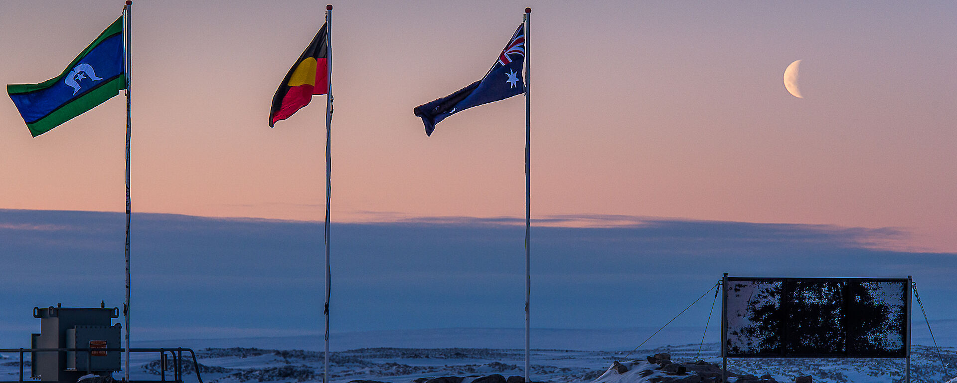 Flag poles with the aboriginal and torres strait Islanders flags flying and moon at Casey