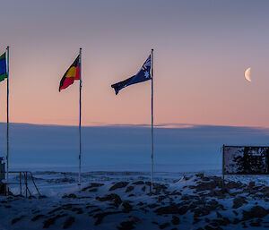 Flag poles with the aboriginal and torres strait Islanders flags flying and moon at Casey