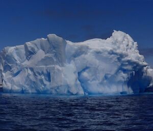 A blue and white iceberg surrounded by water and very blue sky