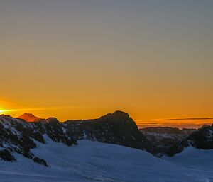 Sunset behind mountains and snow on ground