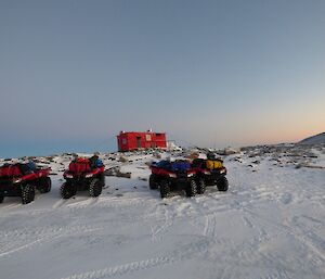 Four quad bikes parked in front of hut.