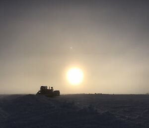 Dozer on the ice with sun behind.