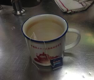 A single cup of tea sitting on a bench top in the kitchen.